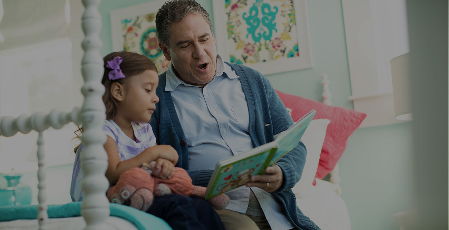 A digestive tract cancer survivor reads a story book to his daughter while sitting on a bed