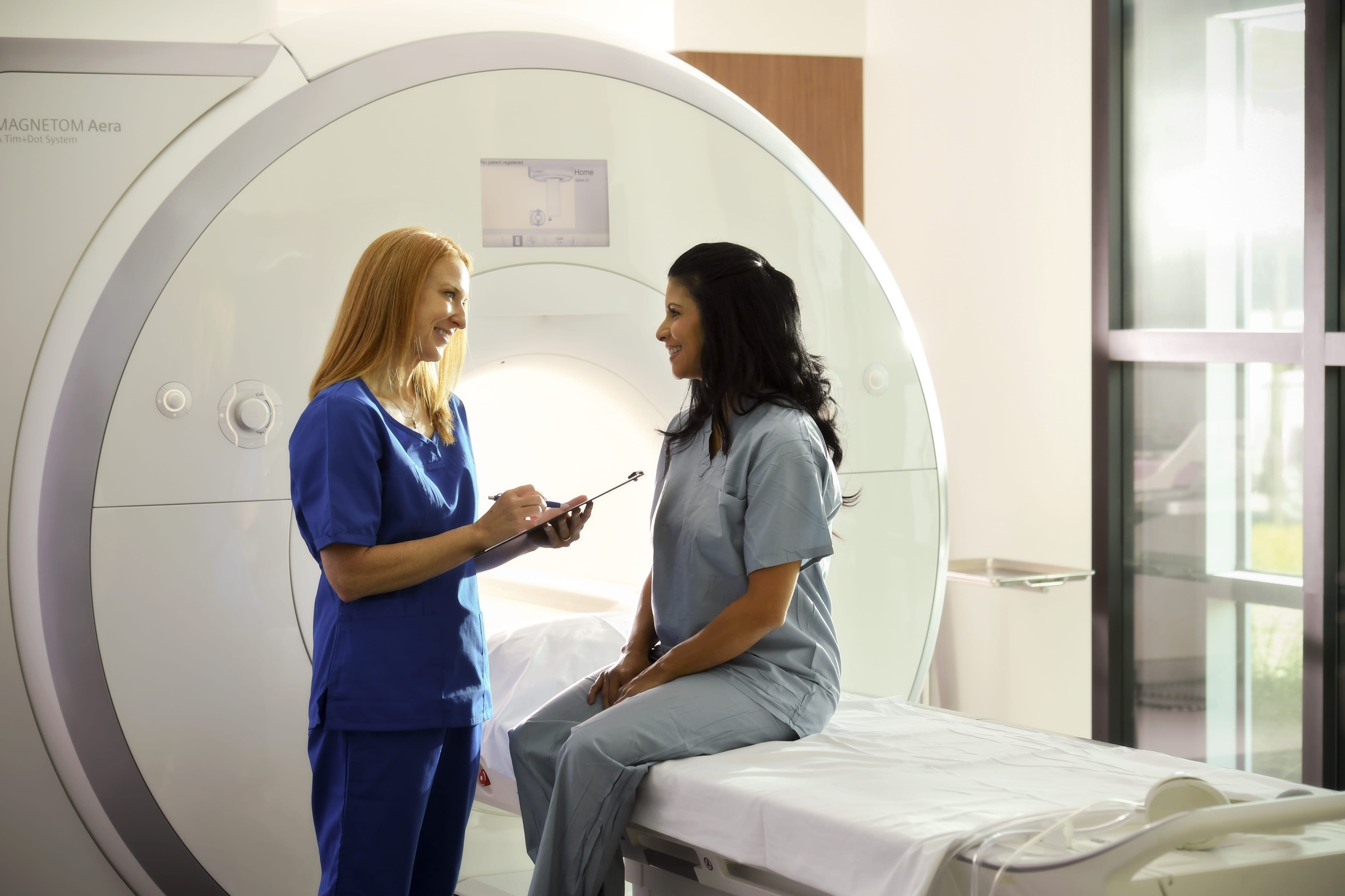 A brain cancer patient and cancer care specialist talk in front of an CT scan machine