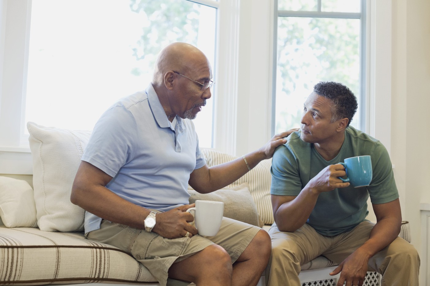 Two men drinking coffee discuss lung and esophageal cancer support groups in a well-lit living room