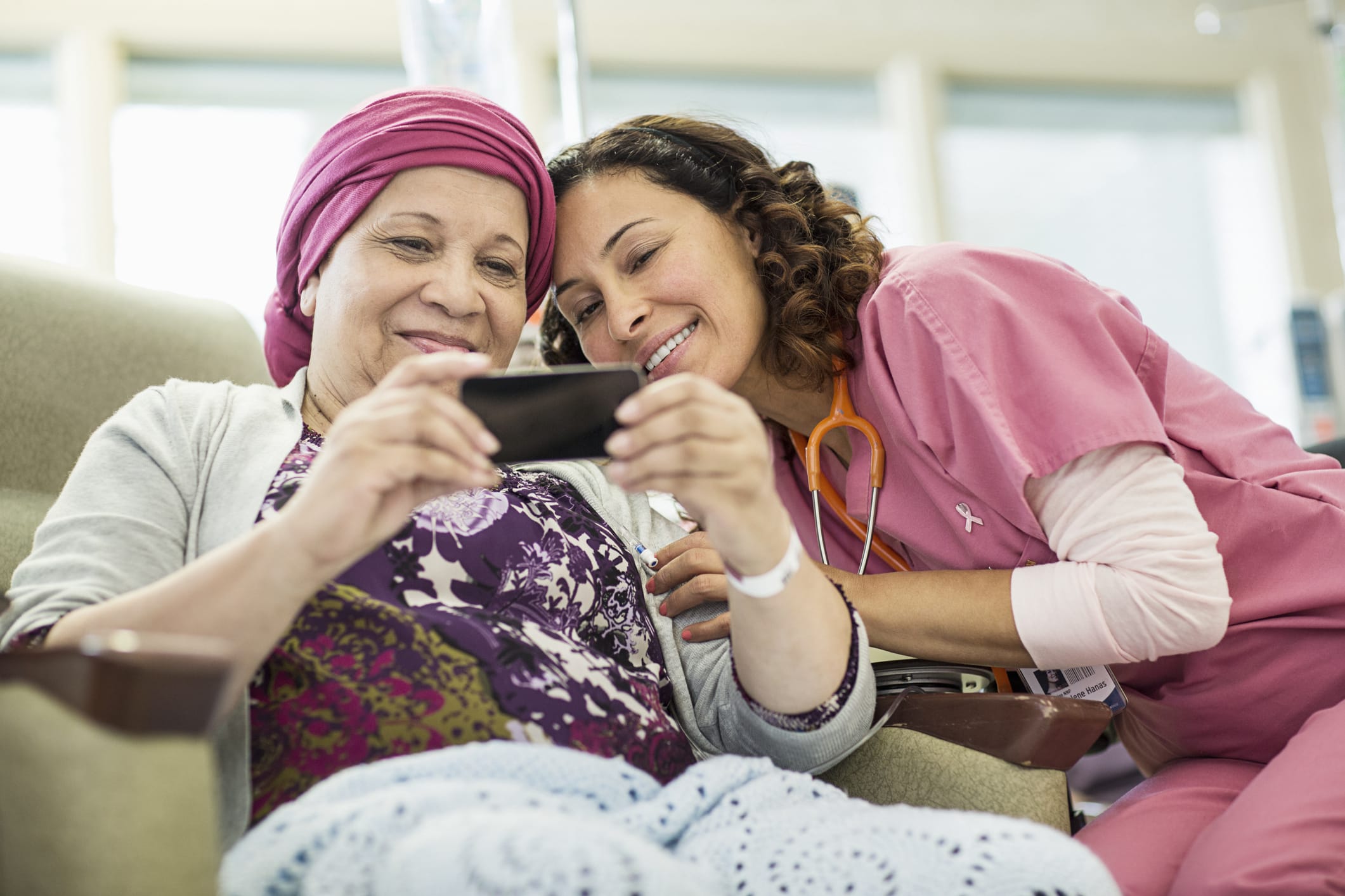 A patient receiving chemotherapy and a cancer treatment specialist look at photos on a phone together 
