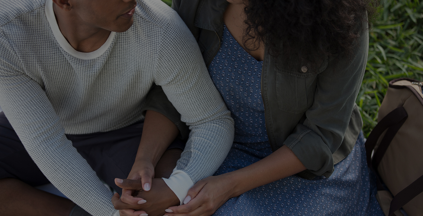 A couple hold hands and discuss the variety of cancer support groups and online resources available at AdventHealth while sitting on the grass